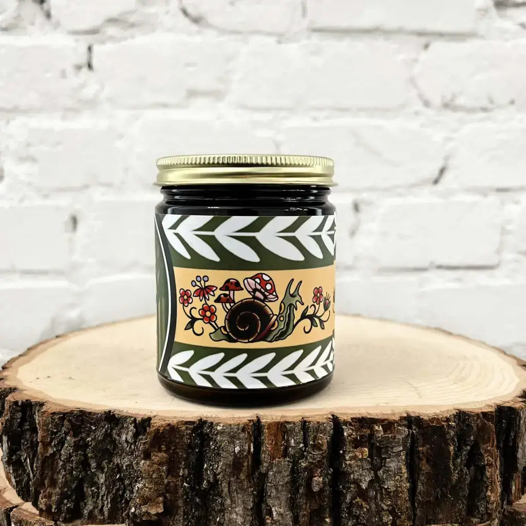 Moss + Meadow candle by Gold Dust Collective with snail, mushrooms, and wildflower tattoo-inspired label in earthy green and gold tones