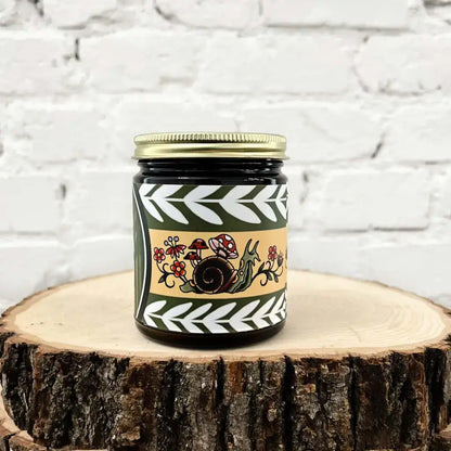 Moss + Meadow candle by Gold Dust Collective with snail, mushrooms, and wildflower tattoo-inspired label in earthy green and gold tones