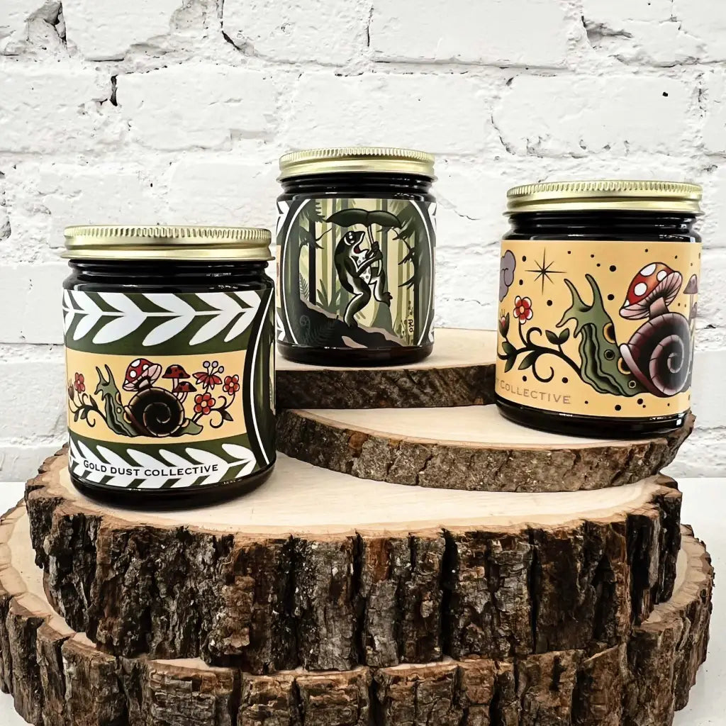 Gold Dust Collective Pacific Northwest candle collection with tattoo-style labels featuring snails, mushrooms, and forest creatures